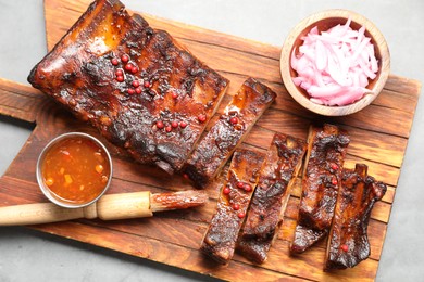 Photo of Delicious spare ribs, sauce, onion and brush on grey table, top view
