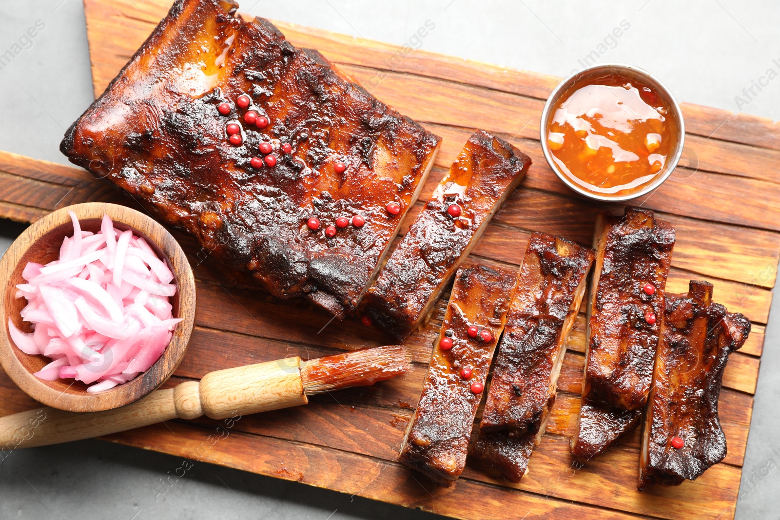Delicious spare ribs, sauce, onion and brush on grey table, top view Photo of Delicious spare ribs, sauce, onion and brush on grey table, top view