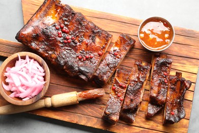 Photo of Delicious spare ribs, sauce, onion and brush on grey table, top view