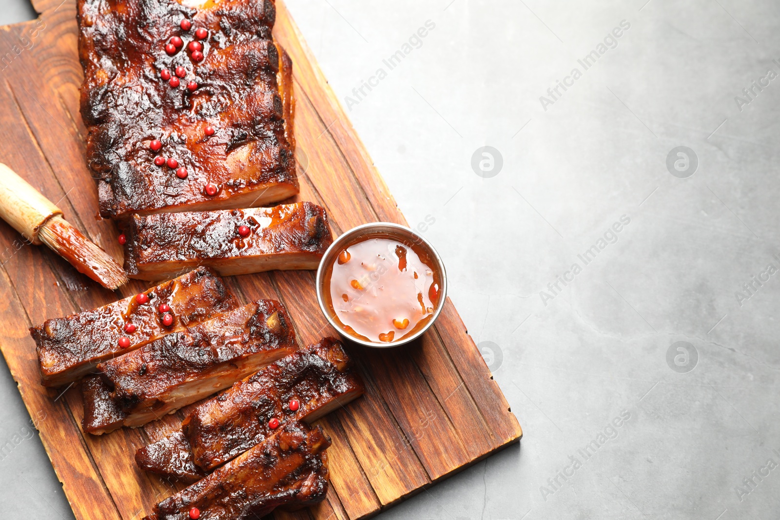 Delicious spare ribs, sauce and brush on grey table, top view. Space for text Photo of Delicious spare ribs, sauce and brush on grey table, top view. Space for text