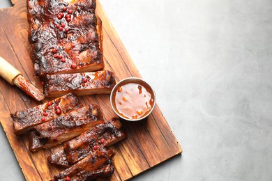 Photo of Delicious spare ribs, sauce and brush on grey table, top view. Space for text