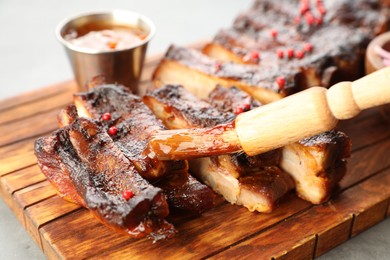 Photo of Spreading sauce with brush onto delicious pork ribs at grey table, closeup