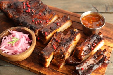 Photo of Delicious pork ribs, sauce and onion on wooden table, closeup