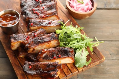 Photo of Delicious pork ribs, arugula, sauce and onion on wooden table, closeup
