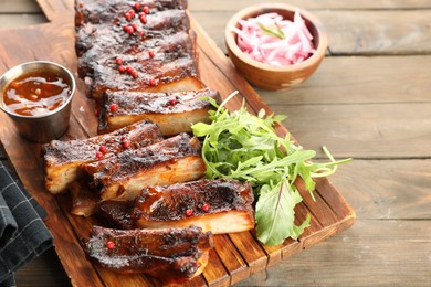 Photo of Delicious pork ribs, arugula, sauce and onion on wooden table, closeup