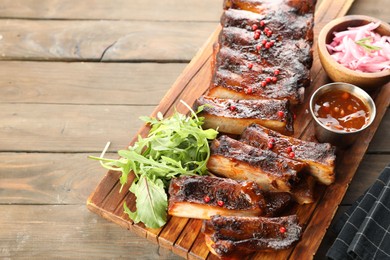 Photo of Delicious pork ribs, arugula, sauce and onion on wooden table, above view