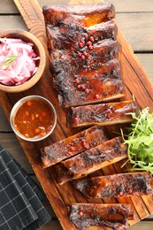 Photo of Delicious pork ribs, arugula, sauce and onion on wooden table, top view