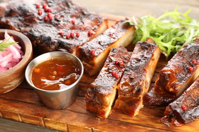 Photo of Delicious pork ribs, arugula, sauce and onion on wooden table, closeup