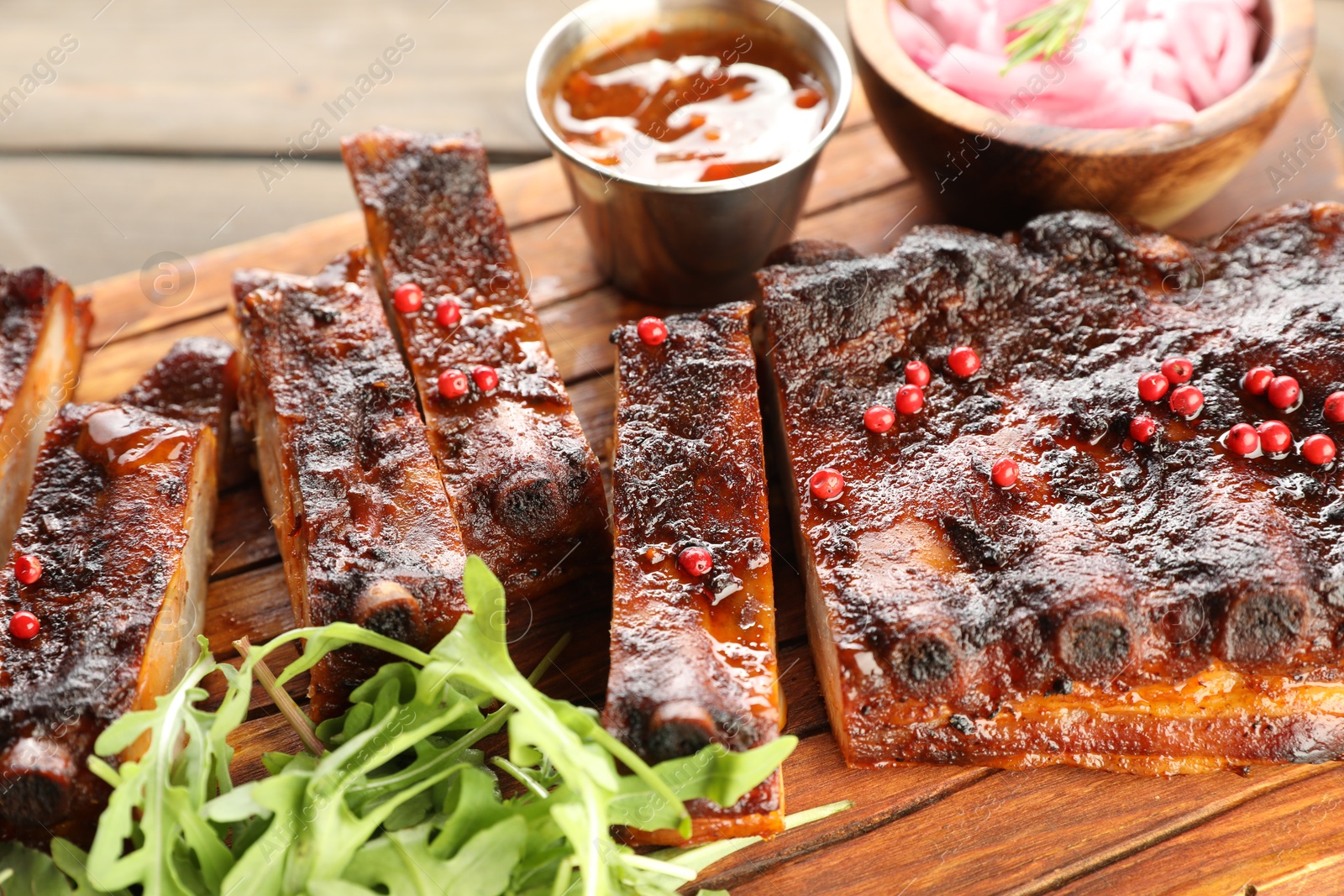 Delicious pork ribs, arugula, sauce and onion on wooden table, closeup Photo of Delicious pork ribs, arugula, sauce and onion on wooden table, closeup