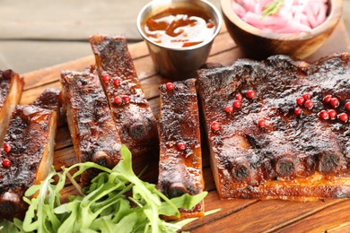 Photo of Delicious pork ribs, arugula, sauce and onion on wooden table, closeup