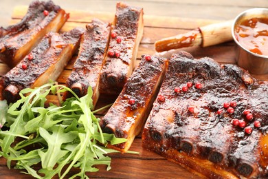 Photo of Delicious pork ribs, arugula, sauce and onion on wooden table, closeup