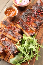 Photo of Delicious pork ribs, arugula, sauce and onion on wooden table, above view