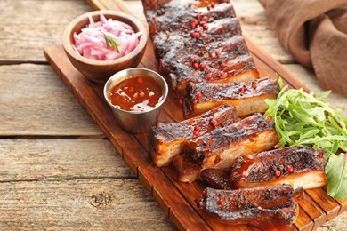 Photo of Delicious pork ribs, arugula, sauce and onion on wooden table, closeup