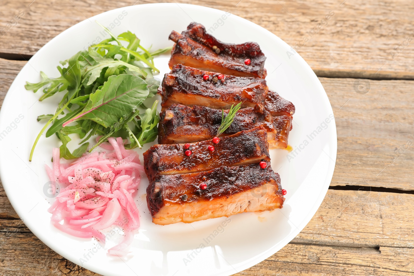 Delicious pork ribs, arugula and onion on wooden table, closeup Photo of Delicious pork ribs, arugula and onion on wooden table, closeup