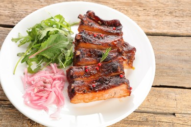 Photo of Delicious pork ribs, arugula and onion on wooden table, closeup