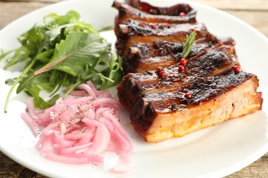 Photo of Delicious pork ribs, arugula and onion on wooden table, closeup