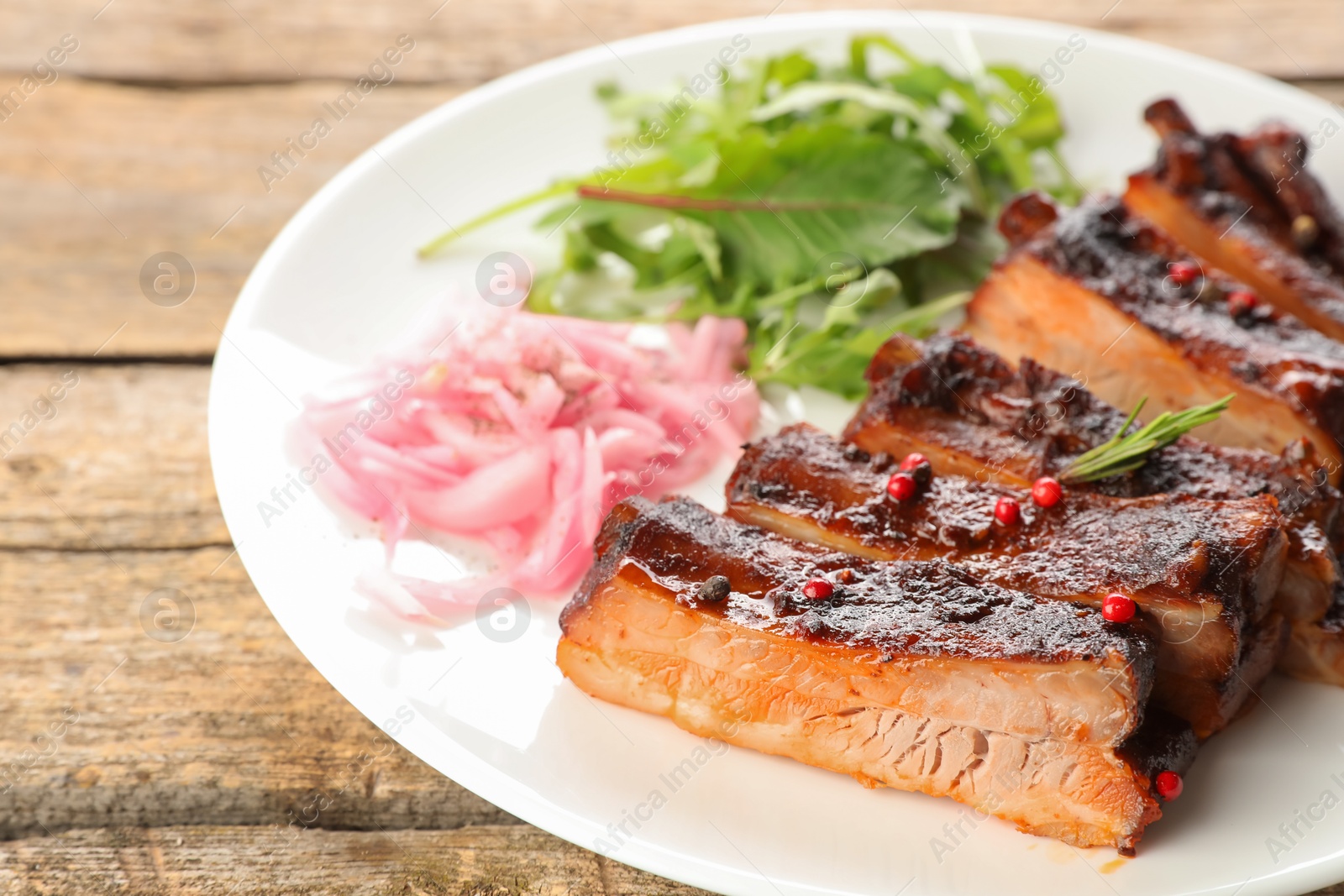 Delicious pork ribs, arugula and onion on wooden table, closeup Photo of Delicious pork ribs, arugula and onion on wooden table, closeup