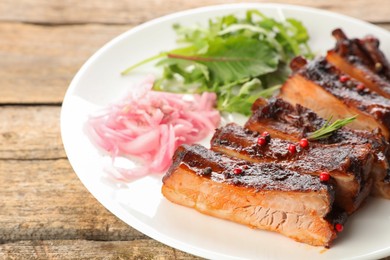 Photo of Delicious pork ribs, arugula and onion on wooden table, closeup