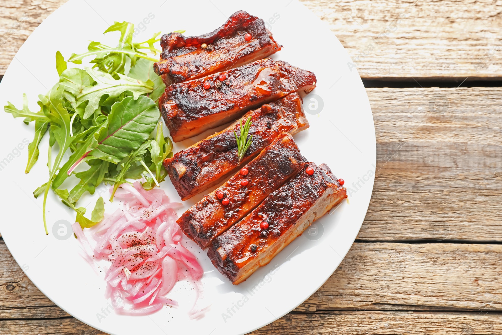 Delicious pork ribs, arugula and onion on wooden table, top view Photo of Delicious pork ribs, arugula and onion on wooden table, top view