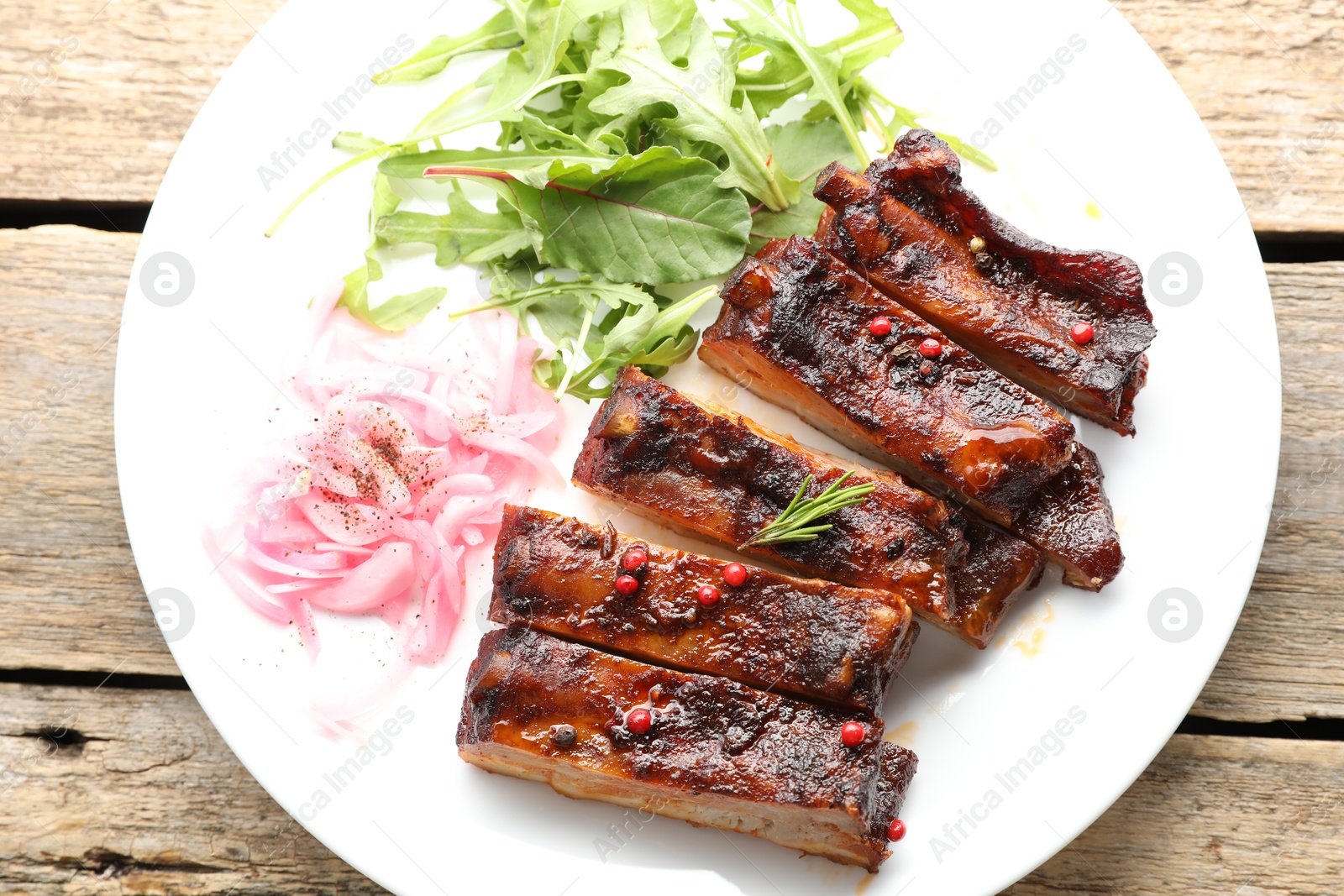 Delicious pork ribs, arugula and onion on wooden table, top view Photo of Delicious pork ribs, arugula and onion on wooden table, top view