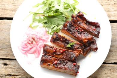 Photo of Delicious pork ribs, arugula and onion on wooden table, top view
