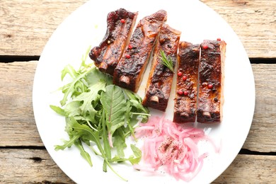 Photo of Delicious pork ribs, arugula and onion on wooden table, top view