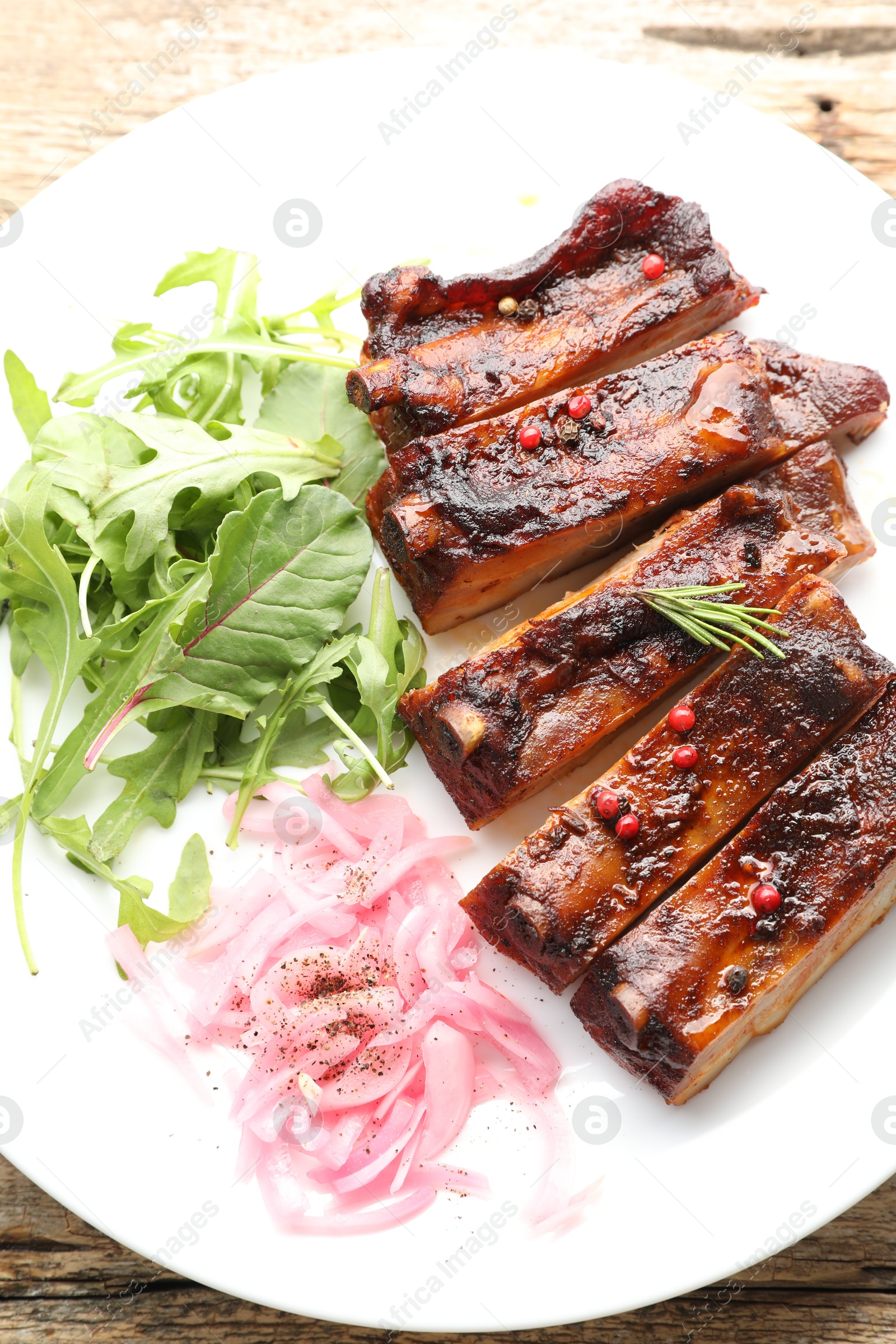 Delicious pork ribs, arugula and onion on wooden table, top view Photo of Delicious pork ribs, arugula and onion on wooden table, top view