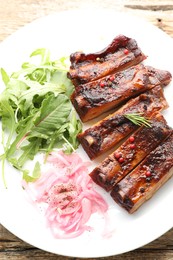 Photo of Delicious pork ribs, arugula and onion on wooden table, top view