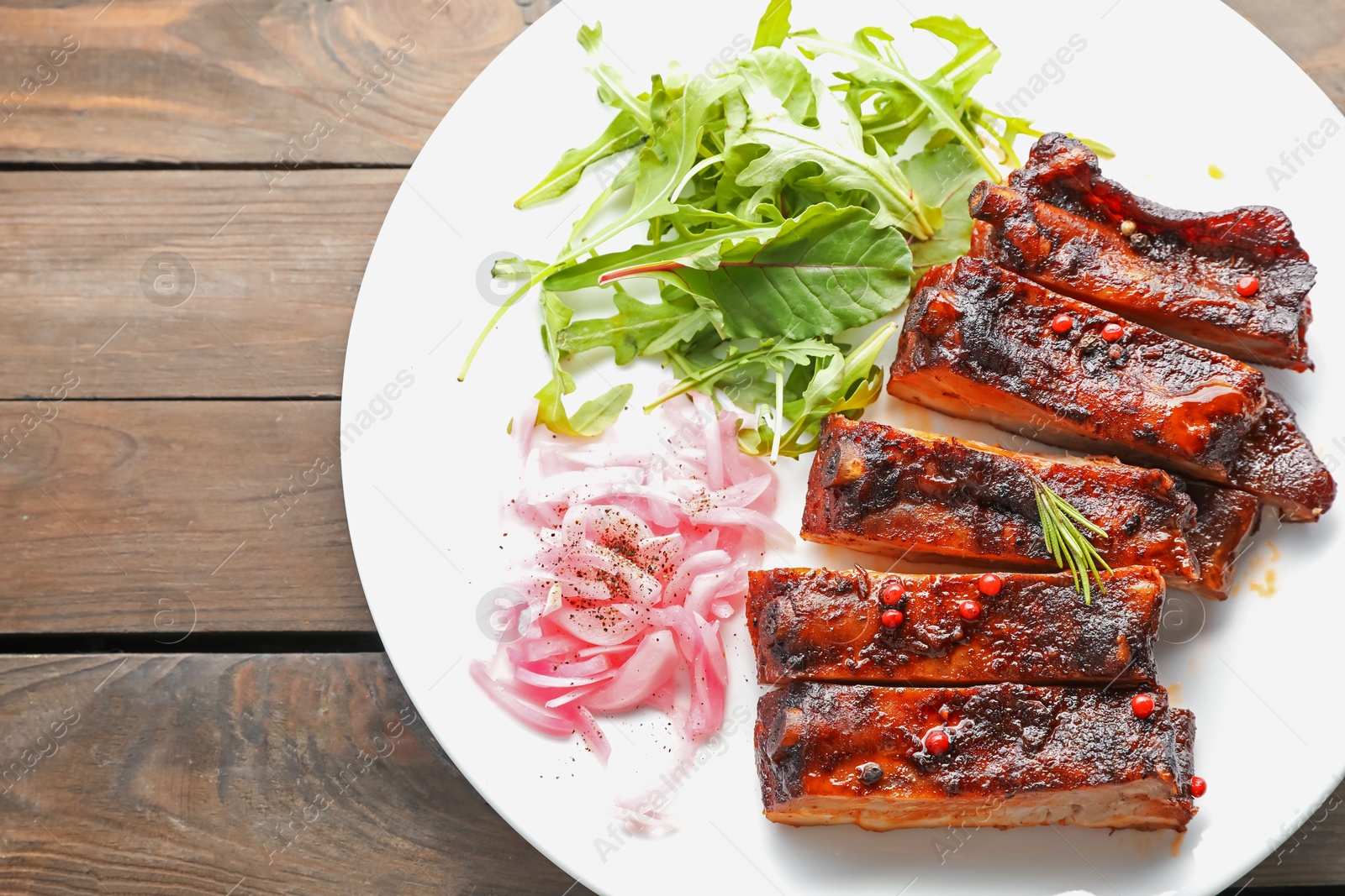 Delicious pork ribs, arugula and onion on wooden table, top view Photo of Delicious pork ribs, arugula and onion on wooden table, top view