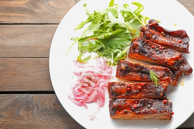 Photo of Delicious pork ribs, arugula and onion on wooden table, top view