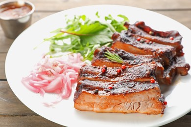 Photo of Delicious pork ribs, arugula and onion on wooden table, closeup