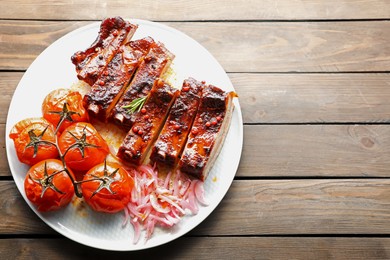 Photo of Delicious pork ribs, sun dried tomatoes and onion on wooden table, top view. Space for text