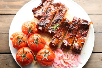 Photo of Delicious pork ribs, sun dried tomatoes and onion on wooden table, top view