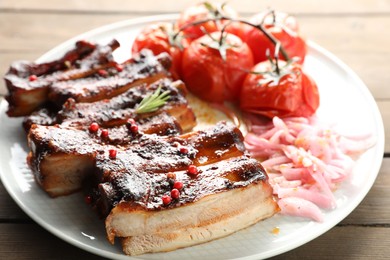 Photo of Delicious pork ribs, sun dried tomatoes and onion on wooden table, closeup