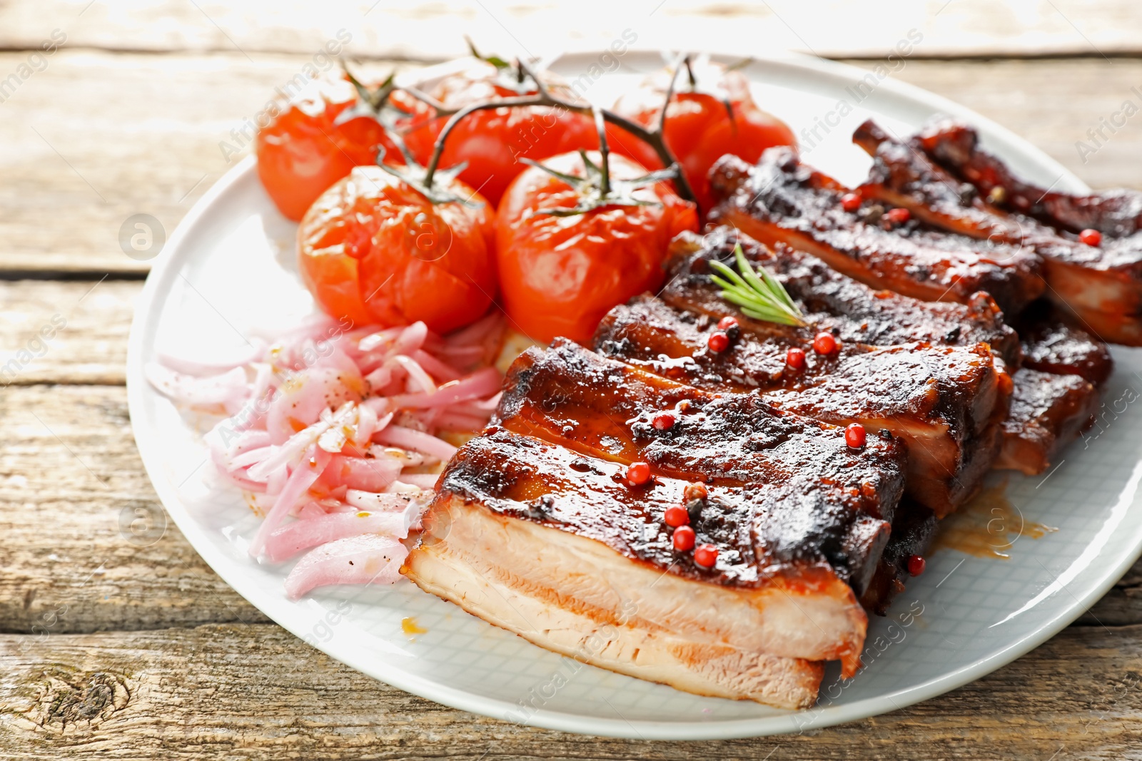 Delicious pork ribs, sun dried tomatoes and onion on wooden table, closeup Photo of Delicious pork ribs, sun dried tomatoes and onion on wooden table, closeup
