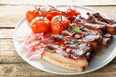 Photo of Delicious pork ribs, sun dried tomatoes and onion on wooden table, closeup