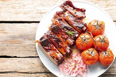 Photo of Delicious pork ribs, sun dried tomatoes and onion on wooden table, top view. Space for text