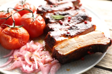Photo of Delicious pork ribs, sun dried tomatoes and onion on wooden table, closeup