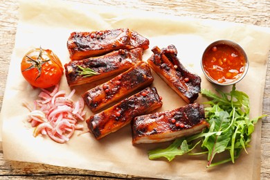 Photo of Delicious pork ribs, sauce, arugula and onion on wooden table, top view
