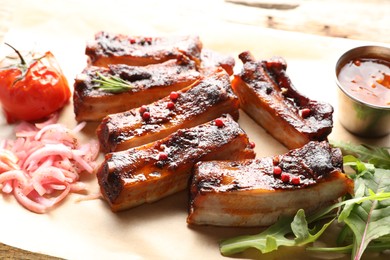 Photo of Delicious pork ribs, sauce, arugula and onion on table, closeup