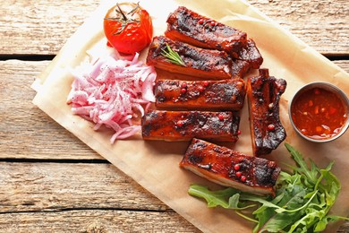 Photo of Delicious pork ribs, sauce, arugula and onion on wooden table, top view