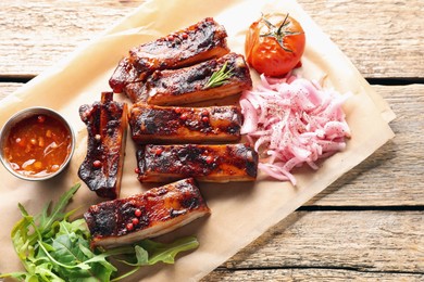 Photo of Delicious pork ribs, sauce, arugula and onion on wooden table, top view