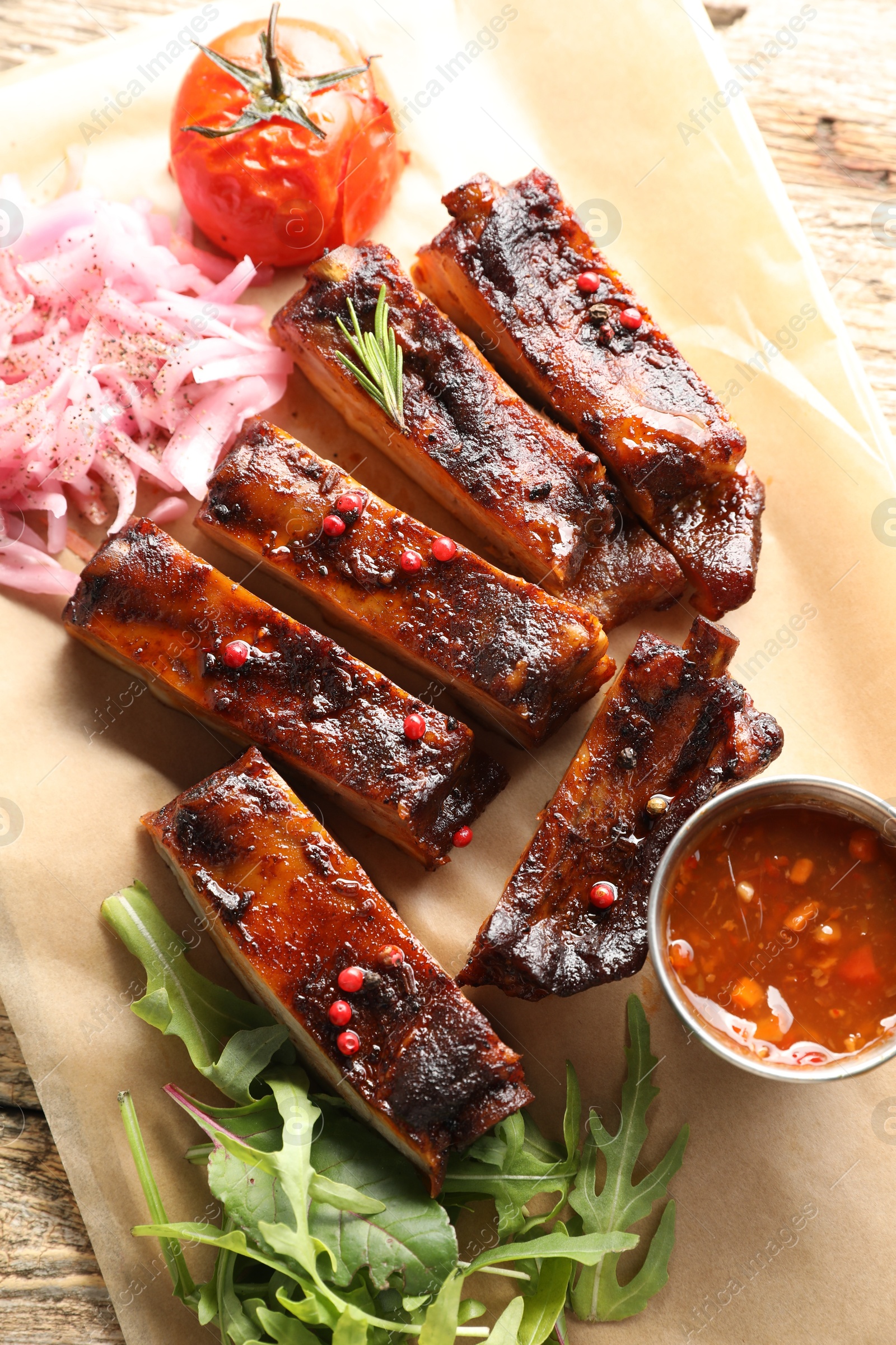 Delicious pork ribs, sauce, arugula and onion on wooden table, top view Photo of Delicious pork ribs, sauce, arugula and onion on wooden table, top view