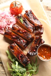 Photo of Delicious pork ribs, sauce, arugula and onion on wooden table, top view