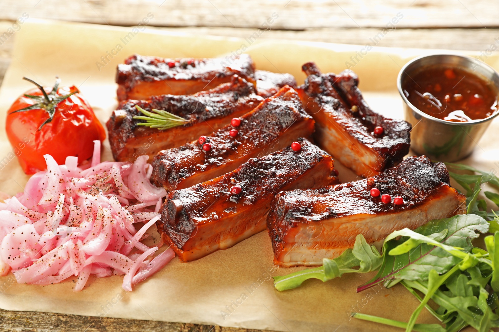 Delicious pork ribs, sauce, arugula and onion on wooden table, closeup Photo of Delicious pork ribs, sauce, arugula and onion on wooden table, closeup