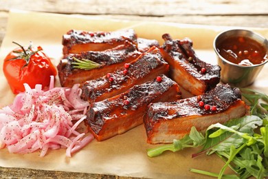 Photo of Delicious pork ribs, sauce, arugula and onion on wooden table, closeup