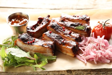 Photo of Delicious pork ribs, sauce, arugula and onion on wooden table, closeup