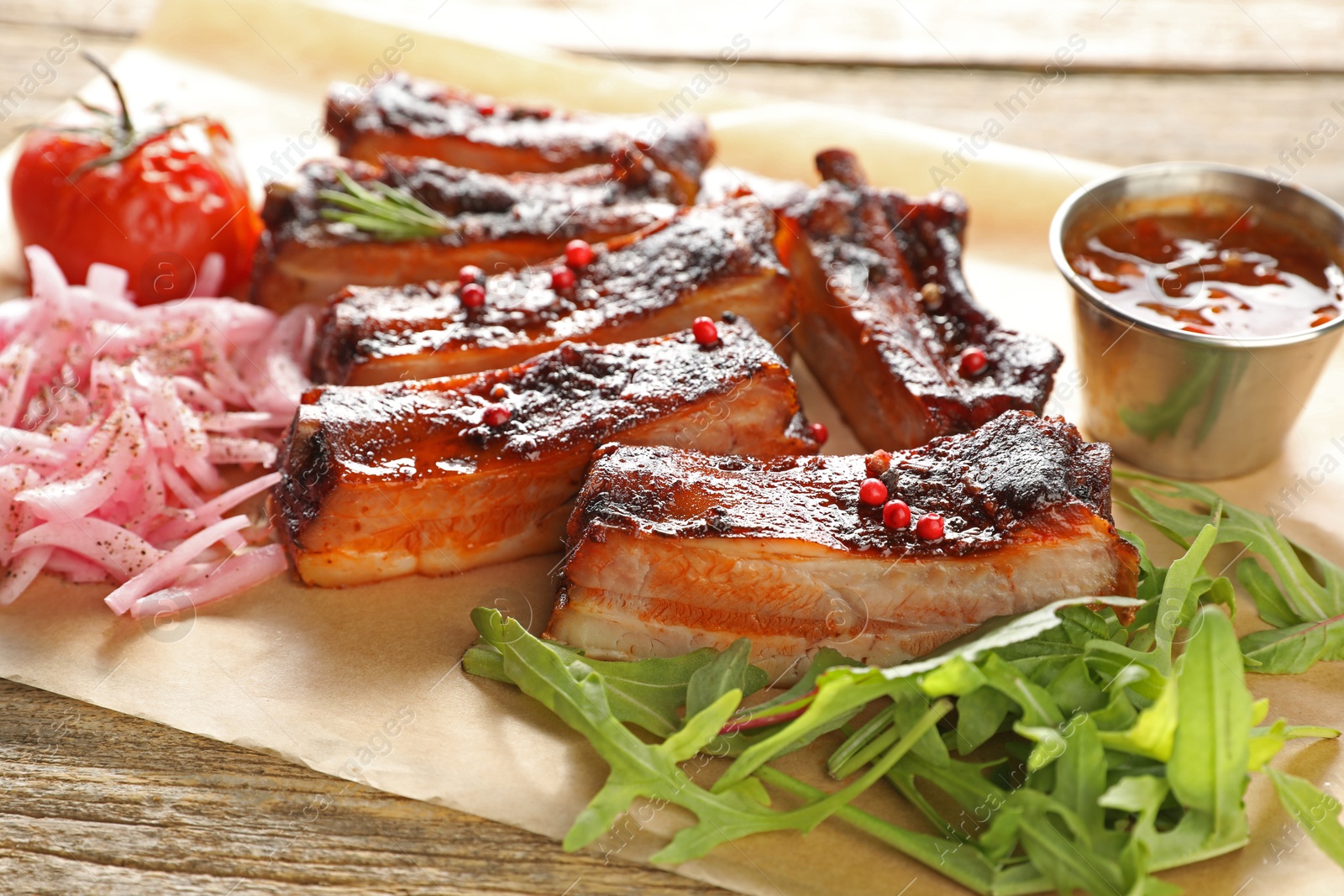 Delicious pork ribs, sauce, arugula and onion on wooden table, closeup Photo of Delicious pork ribs, sauce, arugula and onion on wooden table, closeup