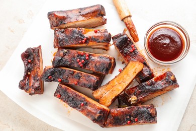 Photo of Delicious pork ribs, sauce and brush on grey table, top view