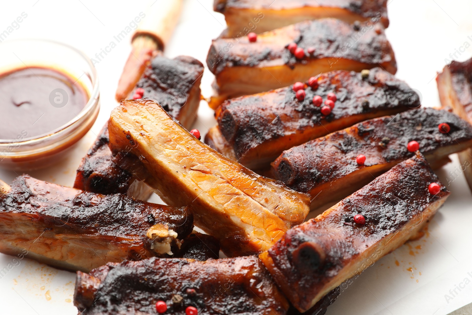 Photo of Delicious pork ribs and sauce on parchment paper, closeup